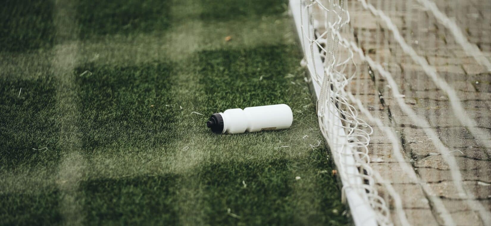 Voetballer drinkt uit een bidon tijdens een korte onderbreking op het veld