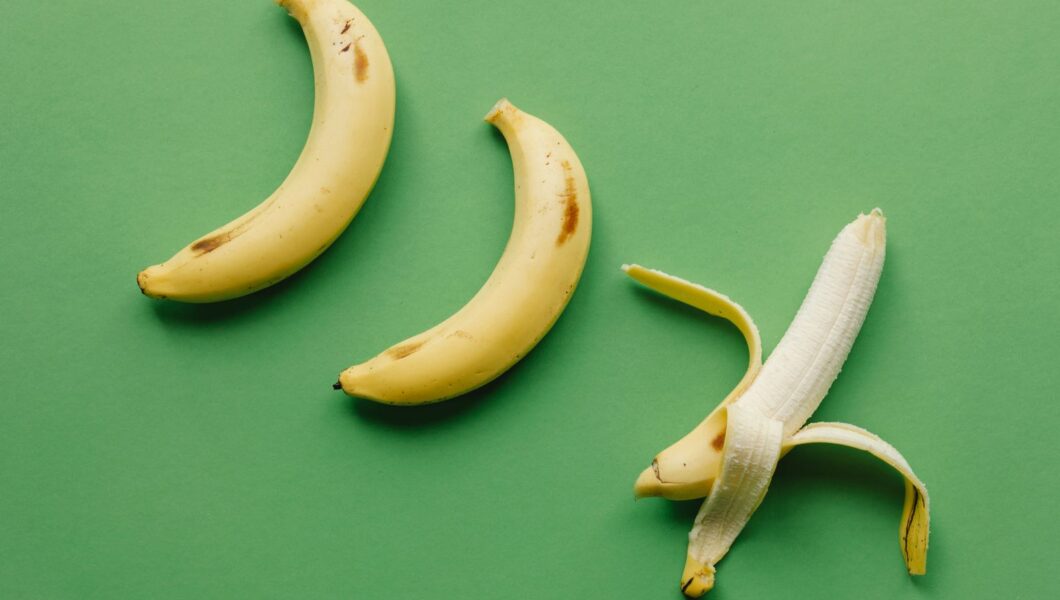 Bananen, waarvan één gepeld, op een groene achtergrond