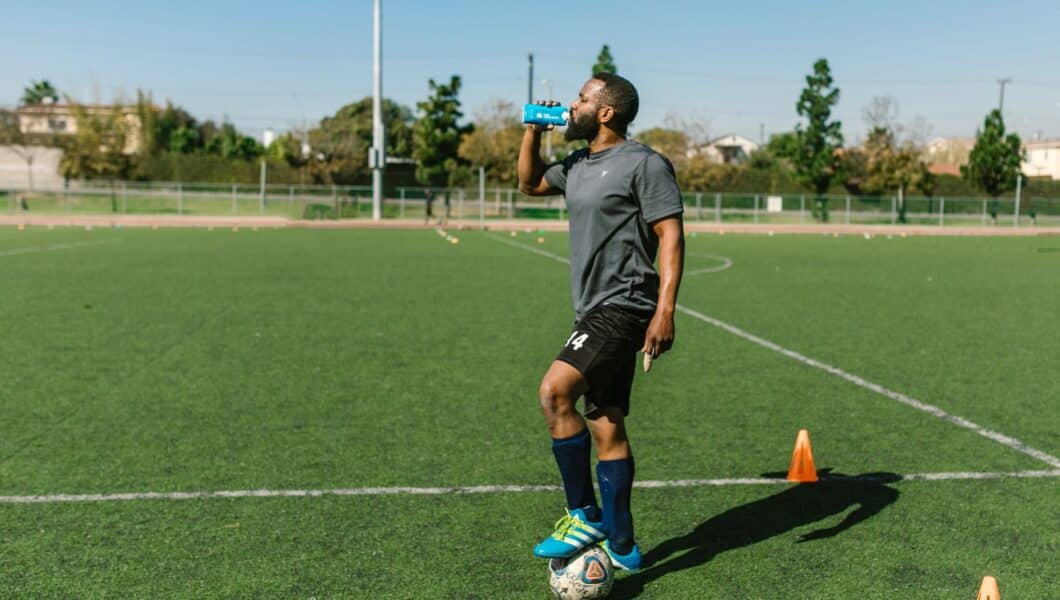 Voetballer drinkt water uit een bidon op het veld
