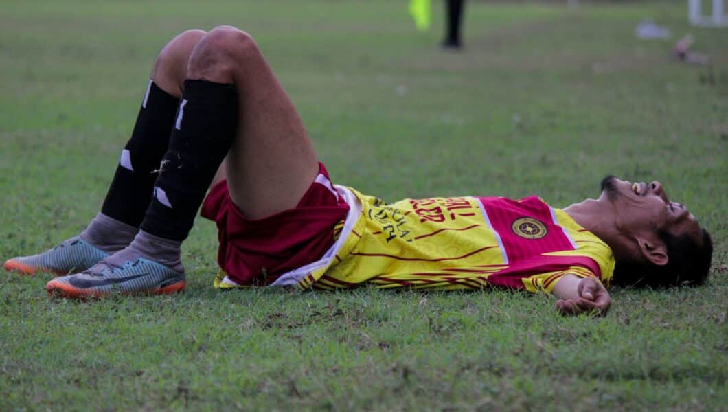 Vermoeide voetballer zit uitgeput op het veld na een intensieve wedstrijd