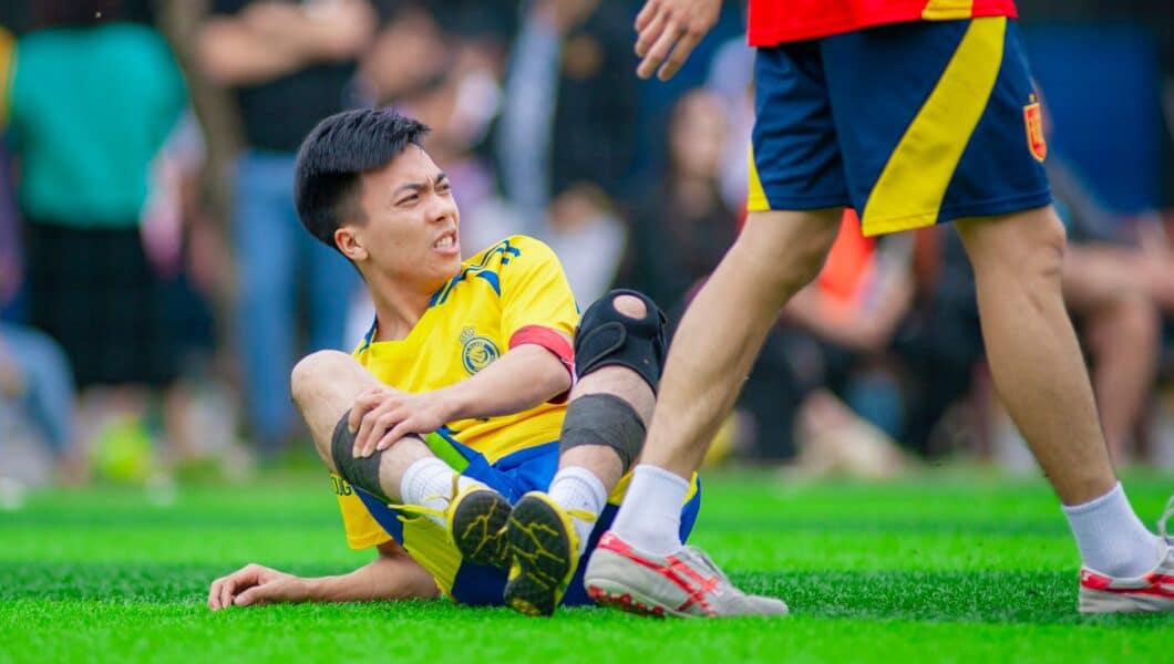 Voetballer grijpt naar zijn knie na een blessuremoment tijdens een wedstrijd