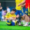 Voetballer zit op het veld met zijn hand op zijn bovenbeen