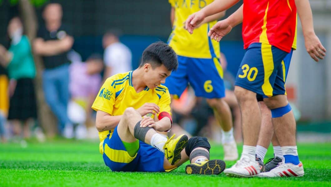 Voetballer zit op het veld met zijn hand op zijn bovenbeen
