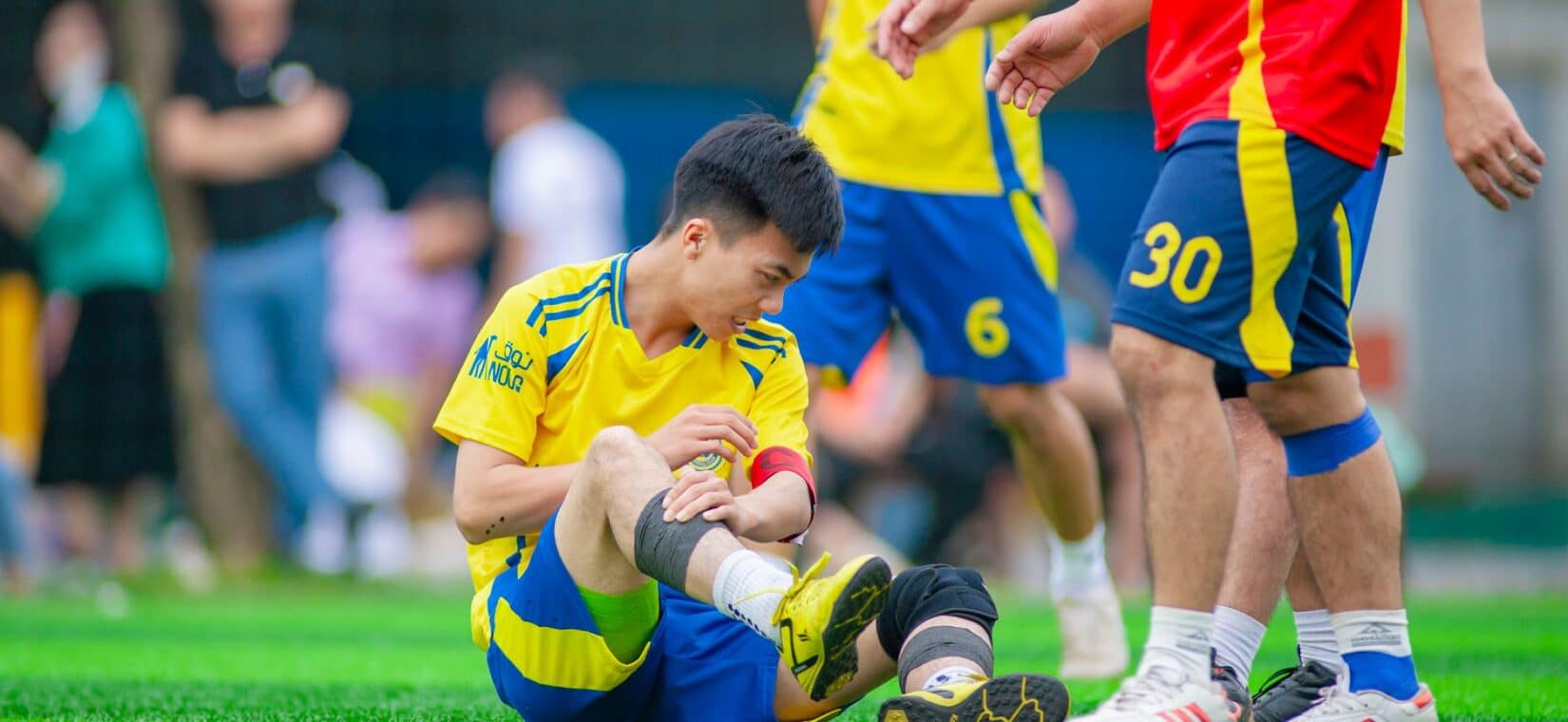 Voetballer zit op het veld met zijn hand op zijn bovenbeen