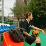 Voetballer zit met een jas om zich heen op de bank langs het veld