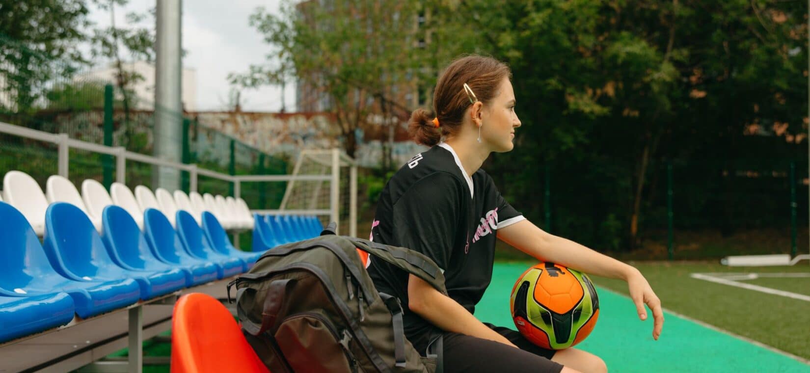 Voetballer zit met een jas om zich heen op de bank langs het veld