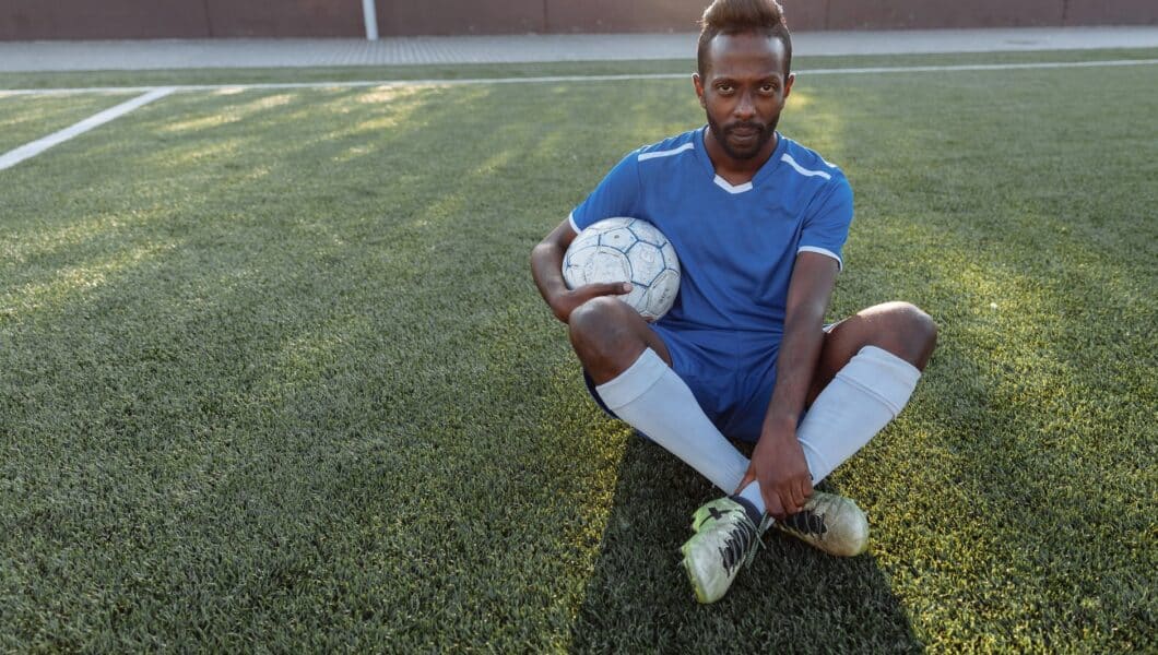 Voetballer met lange sokken zittend op het veld na de training